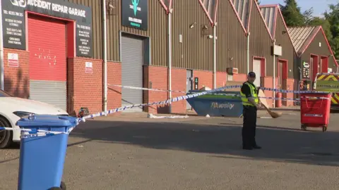 BBC Police officer outside garage which has been surrounded by police tape.