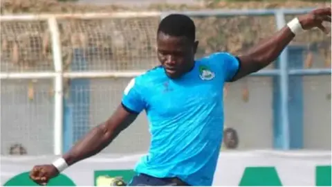 Martins Chineme is seen wearing a sky blue football shirt as he looks down and holds his arms out for balance before kicking a ball