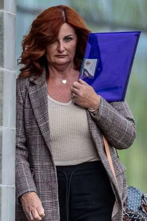 Andrew Price/Viewfinder Pictures Kershaw is holding a blue plastic wallet with paper inside. She has red hair and is wearing a jacket as she walks by a court.