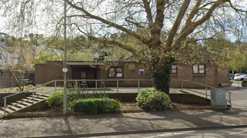 Newton Abbot Magistrates Court. A red brick late 20th century building with large wooden doors to the left hand side, and a large tree in front of it.