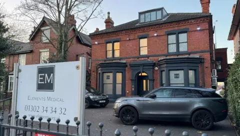 BBC Elements Medical's clinic is a red-brick two-storey building with a room in the roof space. There is a small car park at the front and a sign saying "Elements Medical"