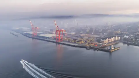 Stephen Lipton A river with a town and cranes with a smoke haze seen hanging over the river and buildings.