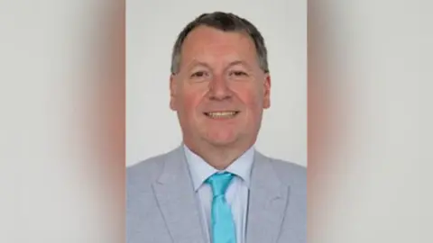 An image of a man in a suit wearing a turquoise tie. 