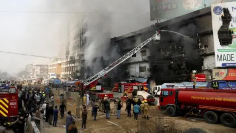 Reuters Smoke rises as firefighters spray water to extinguish a massive fire that broke out in the Gul Plaza Shopping Centre building, in Karachi