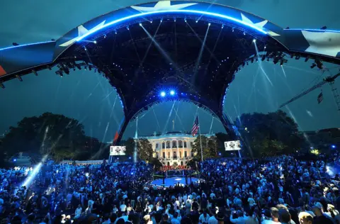Getty Images A wide-angle shot shows the underside of the Claw structure erected on the White House's South Lawn, with a crowd of fans underneath