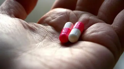 two red and white capsules sit next to each other in the palm of an open hand
