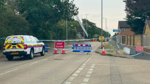 Stephen Huntley/BBC Part of a road closed off. Blue and white striped tape acts as a cordon and there are road and footway closure signs propped up on the ground. A Network Rail response unit van is parked outside of the cordon.