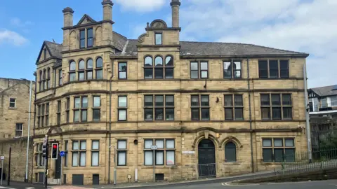 A large building on the edge of a road, with a traffic light in front of the entrance 