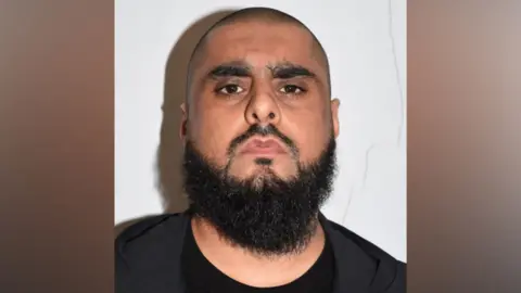 Man with shaven hair and dark beard in black clothing