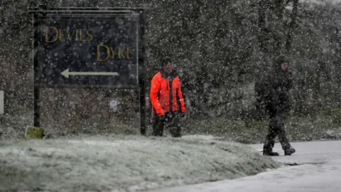 Eddie Mitchell Two men walk past a sign saying Devil's Dyke while snow falls