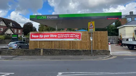 Asda petrol station with large fence and sign promoting petrol price savings of 5p per litre