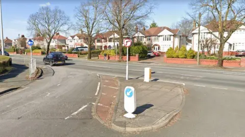 Google A view of a road T-junction, where cars are instructed to only turn left. in the traffic island, there's no right turn sign. On the other side of the road, there are houses.