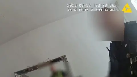 GMP A still images has been taken from the police body-worn camera footage. It shows a police officer standing in her living room. Parts of the image have been blurred to conceal the officer's and woman's identities. 