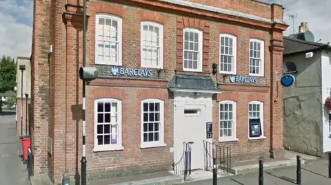 Google A branch of Barclays bank which is a two storey building with a white door and white framed windows with a cashpoint outside.