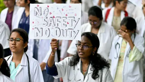 Doctors hold a poster to protest the rape and murder of a young medic from Kolkata, at the Government General Hospital in Vijayawada on August 14, 2024. Indian doctors in government hospitals across several states halted elective services "indefinitely" on August 12, to protest the rape and murder of a young medic. (Photo by Idrees MOHAMMED / AFP) (Photo by IDREES MOHAMMED/AFP via Getty Images)