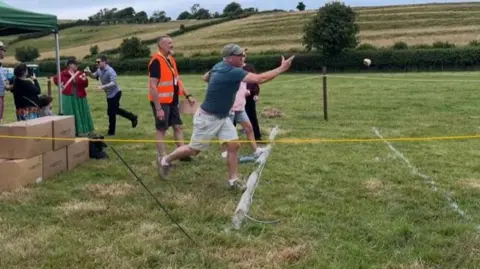 A man stands at a marker and hurls an item. One arm is extended and one of his feet is off the ground. 