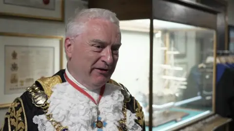 Portsmouth's Lord Mayor Gerald Vernon-Jackson in all his ceremonial get-up. He has short white hair and is wearing a black and gold coat with a white ruff and a medal over it.