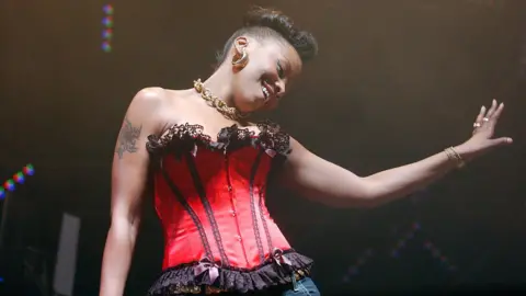 A woman in a red corset dances on a stage.