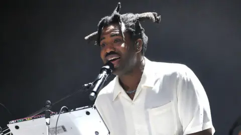 Getty Images Sampha performing on stage wearing a white shirt.