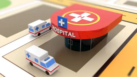 A photo of a model of a hospital with toy ambulances outside