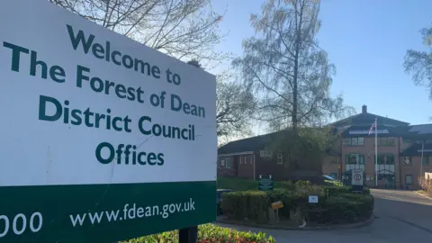 The sign for the Forest of Dean District Council Offices, with the council office behind it.