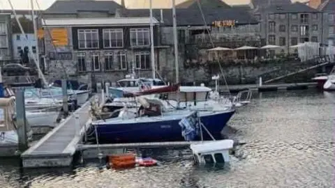 Neal Stoneman The cabin of a fishing boat can just been seen above the water in a harbour. There is a wooden jetty and other boats to the side and behind it.
