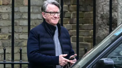 Peter Mandelson walking to his car wearing a casual jacket and grey jumper