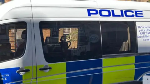 A Metropolitan Police van with a yellow and blue panel and the word Police and We're recruiting posted on the side.