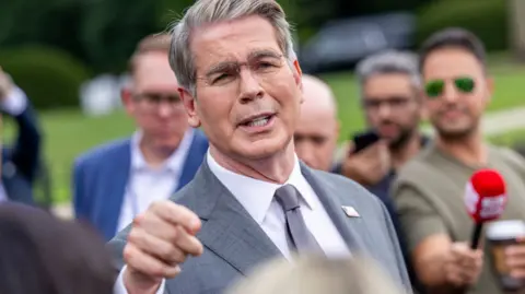 US Treasury Secretary Scott Bessent addresses members of the media on the lawn outside the White House. He's wearing a light grey suit, white shirt and silver tie