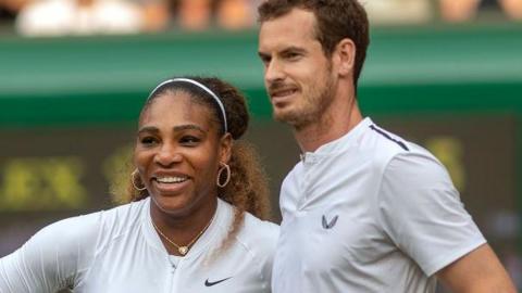 Serena Williams smiles with her hand on her hip and stands next to Andy Murray who is holding a tennis racquet