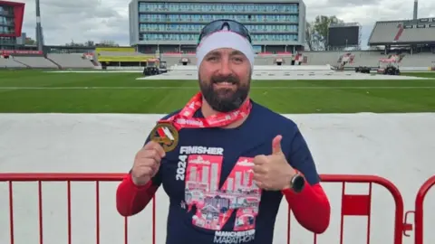 PA Media Nick Passey with dark beard wearing a white headband and blue top with his thumbs up