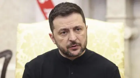 EPA-EFE/REX/Shutterstock Ukrainian President Volodymyr Zelensky, dressed in a black top and sitting on a chair, in the Oval Office
