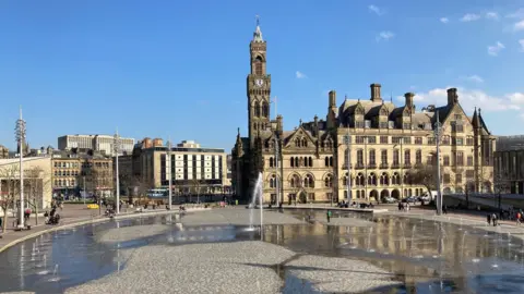 A mirror pool and single fountain in front of Bradford's Victorian City Hall building