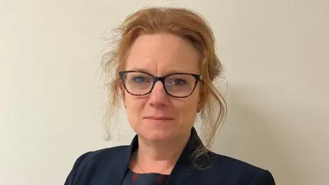 A woman with ginger hair wearing glasses looking into the camera