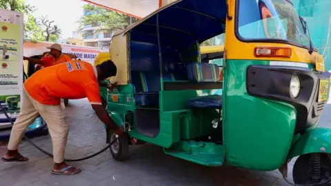A petrol station attendant helps a customer top up his auto rickshaw in India 