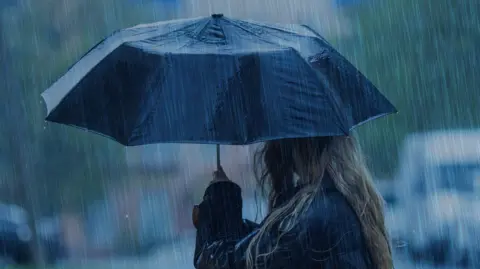 Getty Images A woman holds a black umbrella in a torrential downpour.