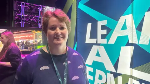 Jessica Bayley / BBC A woman with short hair and a lanyard wearing a top with clouds on