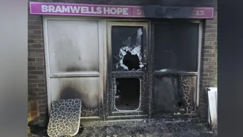 Bramwells Hope The front of a shop which has been badly damaged by fire. It has a pink sign which says Bramwells Hope