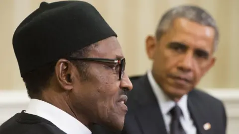AFP via Getty Images Barack Obama is pictured, out of focus, looking at Buhari, who is speaking and staring straight ahead.
