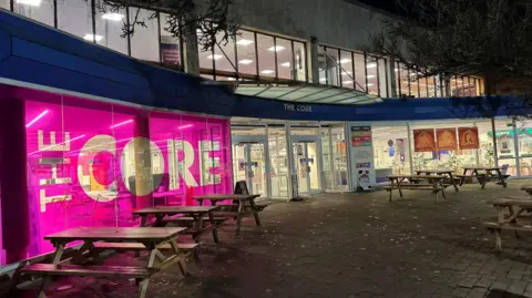 The outside of a theatre with glass windows and two storeys, with a pink glass frontage with lettering that says "The Core".