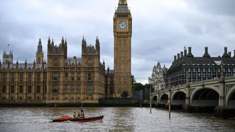 An RNLI rescue boat on the River Thames near the Houses of Parliament, Big Ben and Westminster Bridge in central London.