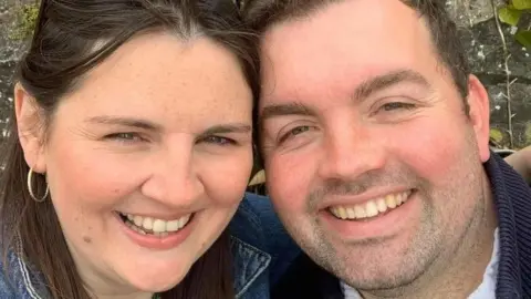 Claire Fleming A couple who are smiling at the camera in a selfie. They both have dark hair. 