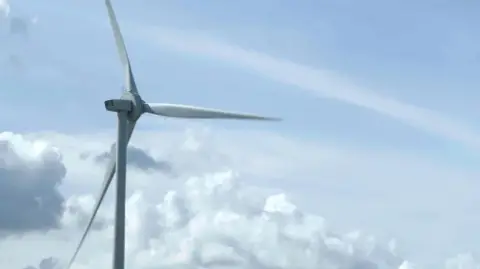 A rotating wind turbine above the clouds with a blue sky in the background.