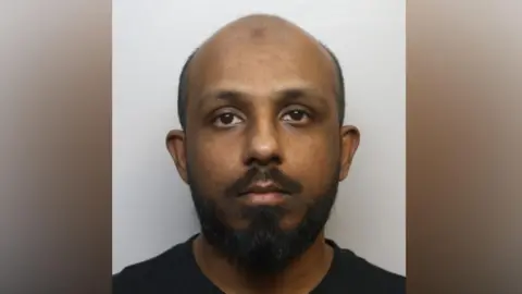 Abusali Rahman has a shaved head and a dark beard. 