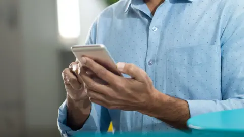 Getty Images A man holds a phone in his hands while wearing a blue shirt