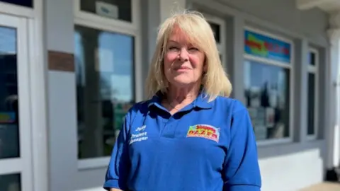 Julie Nicholls, who has shoulder-length blonde hair, smiles at the camera while wearing a blue Sheppey FM polo shirt.