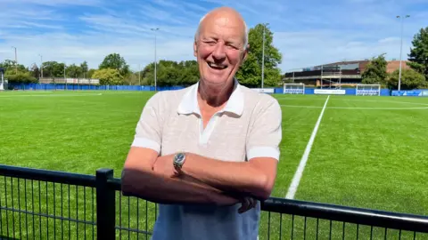 Tom Larsen-Wright/BBC Barry Hearn crosses his arms in front of the new Brentwood Town pitch