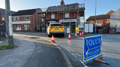 A police car in front of scaffolding on a building with blue sky above