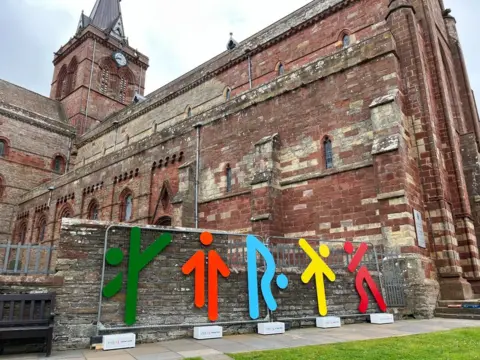 Runic styled sports installation outside red sandstone cathedral.