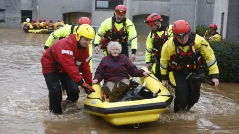 Getty Images Coastguard volunteers carrying an older woman in a yellow raft in flood water in Brechin.